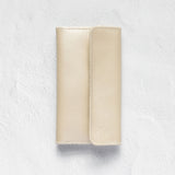 A light beige leather wallet or card holder with a vertical stitched fold, shown flat against a textured white background.