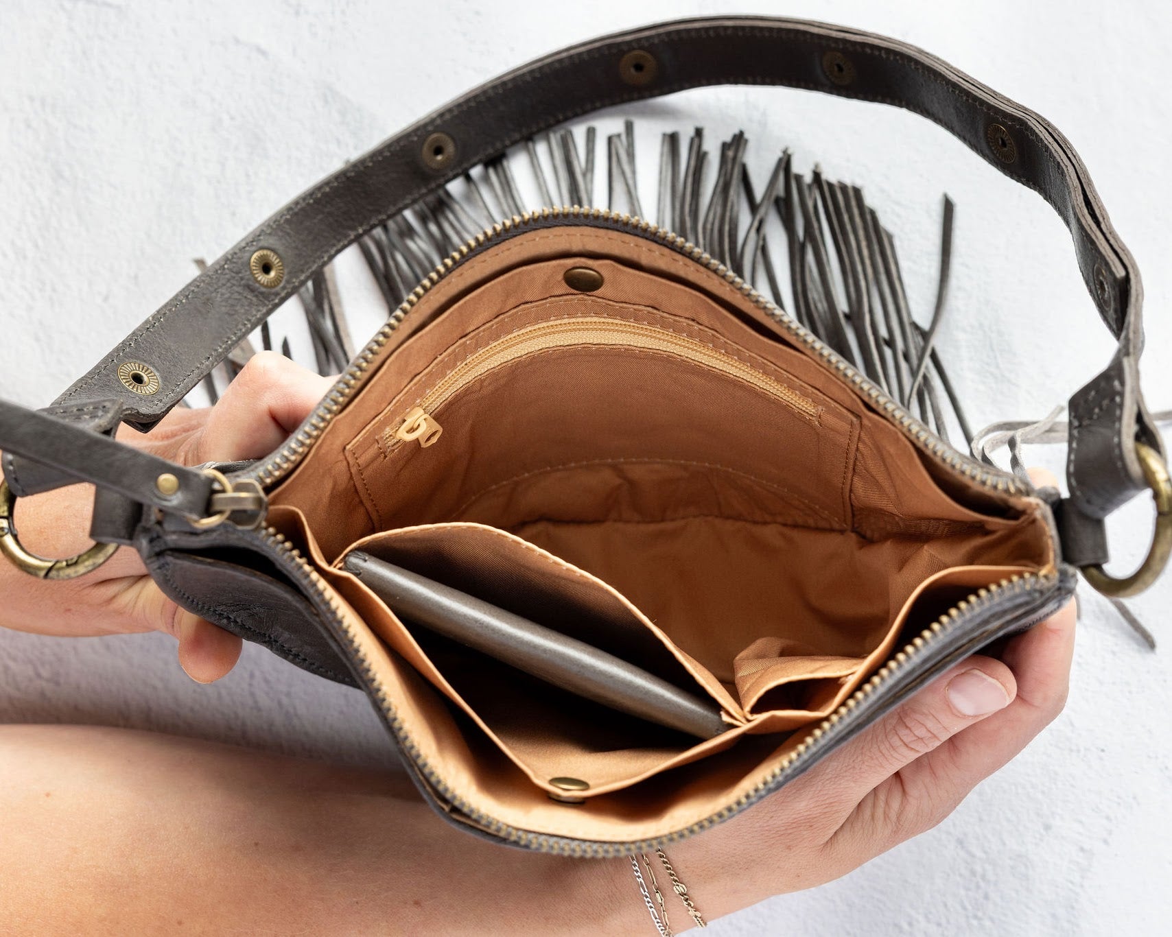 Charcoal leather fringe bag with interior pockets, held by a person against a white background