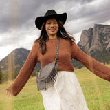 Woman wearing a medium charcoal leather fringe bag outdoors