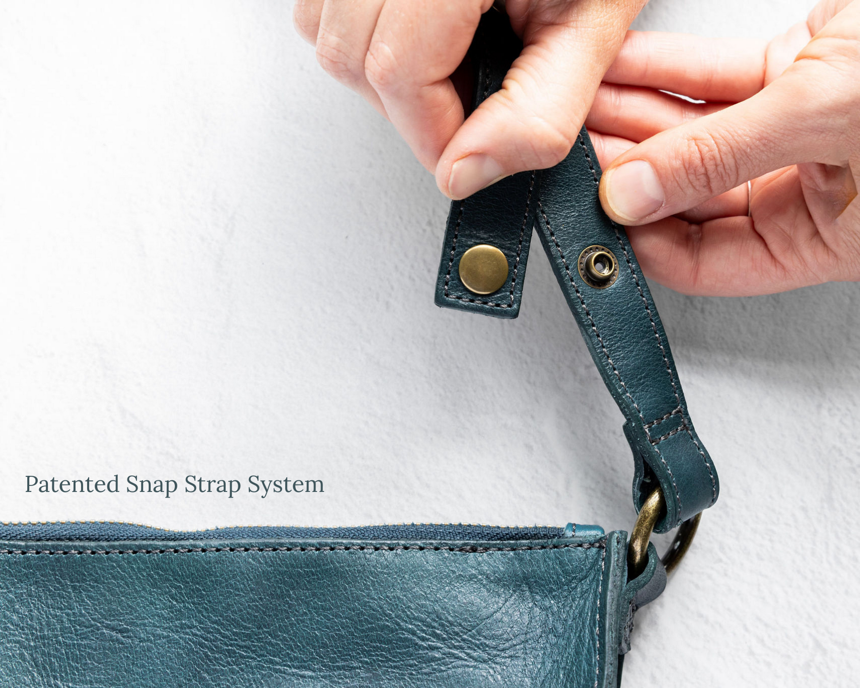 Close-up of hands holding a teal leather strap with metal hardware on a white background