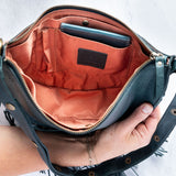 Teal leather fringe bag held open by a hand, showing the Pecan lining, on a white background