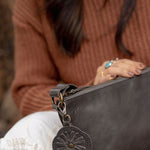 A charcoal leather flower-shaped bag charm with a metal lobster clasp
