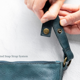 Close-up of hands holding a teal leather strap with metal hardware on a white background