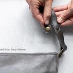 Close-up of hands holding a charcoal leather strap with metal hardware on a white background