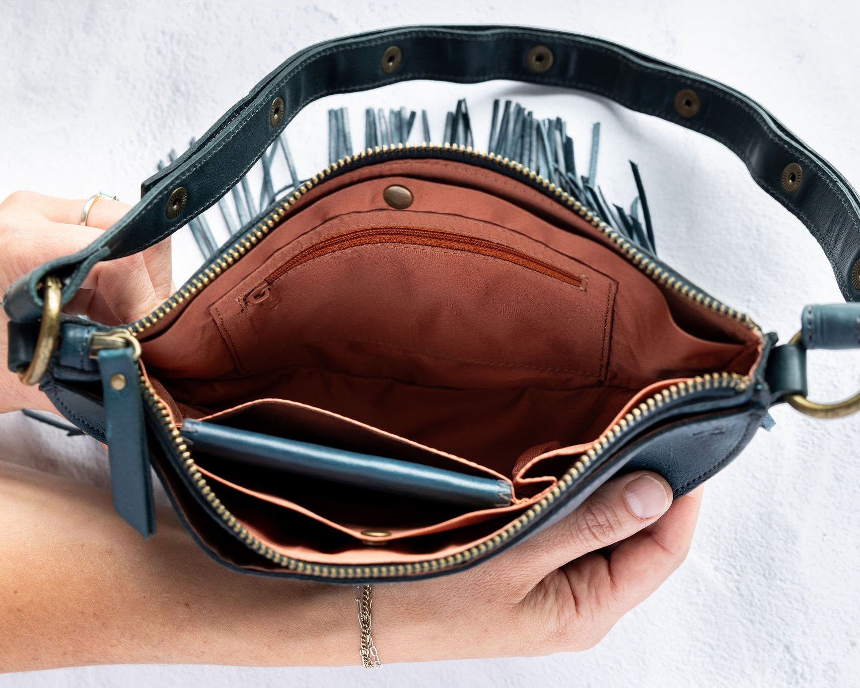 Teal leather fringe bag with interior pockets, held by a person against a white background