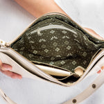 An open cream-colored leather shoulder bag with a patterned olive green and white printed interior lining, held open by hands against a light gray background.