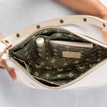An open cream-colored shoulder bag with a patterned olive green interior, held open by two hands against a light gray background.