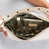 An open cream-colored shoulder bag with a patterned olive green interior, held open by two hands against a light gray background.
