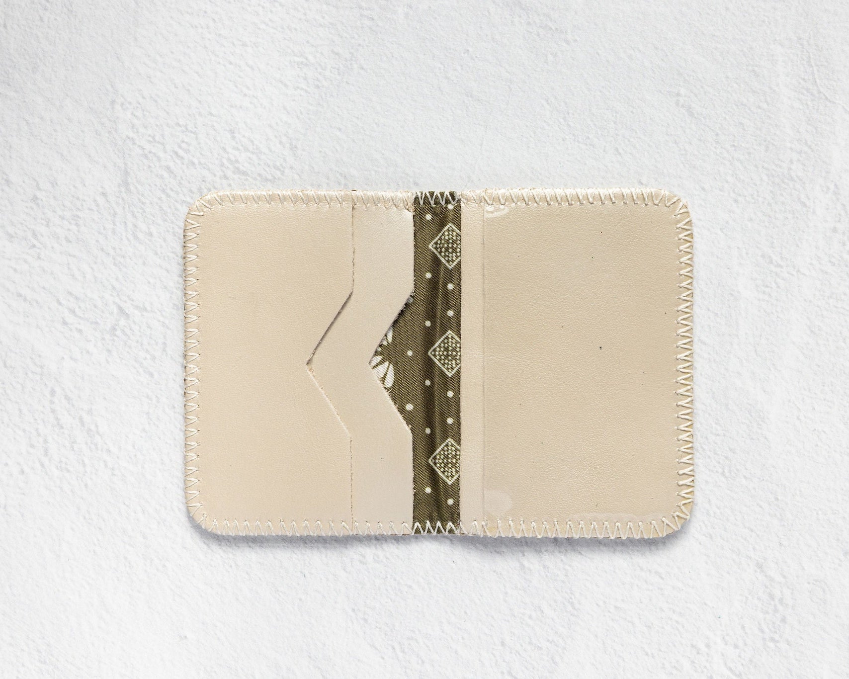 A cream-colored leather card holder wallet with a decorative olive green patterned paper strip inside, displayed flat against a textured white background.