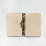 A cream-colored leather card holder wallet with a decorative olive green patterned paper strip inside, displayed flat against a textured white background.