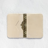 A cream-colored leather card holder wallet with a decorative olive green patterned paper strip inside, displayed flat against a textured white background.