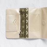 An open cream-colored leather wallet with a central olive green patterned fabric divider, displayed on a textured white background.
