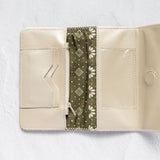 An open cream-colored leather wallet with a central olive green patterned fabric divider, displayed on a textured white background.