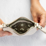 A close-up of a person's hands holding open a small white leather wristlet pouch, showing a dark patterned interior lining with a white geometric print.