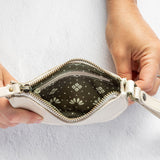 A close-up of a person's hands holding open a small white leather wristlet pouch, showing a dark patterned interior lining with a white geometric print.
