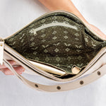 An open cream-colored shoulder bag with a patterned olive green and beige interior lining, held open by a person's hands against a light gray background.