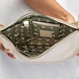 An open cream-colored leather clutch bag held by two hands, showcasing its olive green patterned interior lining with pockets and a zipper closure.