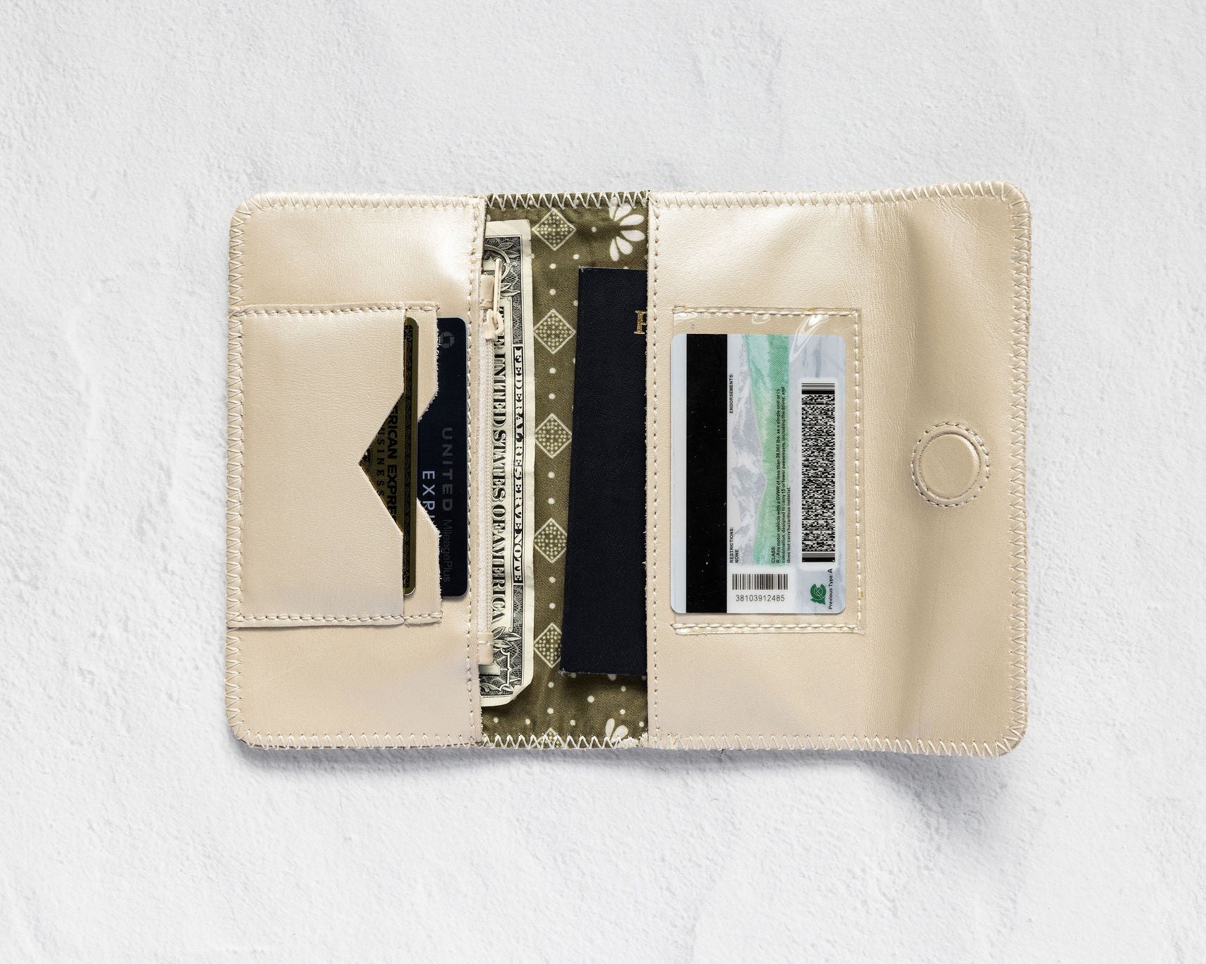 An open cream-colored leather wallet with multiple card slots, a cash compartment, and a patterned center panel, displayed on a textured white background.