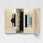 An open cream-colored leather wallet with multiple card slots, a cash compartment, and a patterned center panel, displayed on a textured white background.