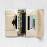 An open cream-colored leather wallet with multiple card slots, a cash compartment, and a patterned center panel, displayed on a textured white background.