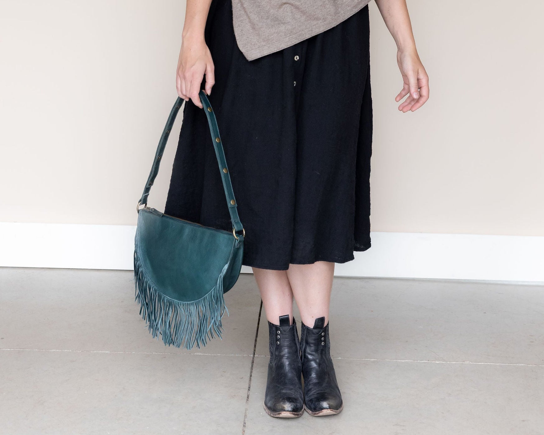 Woman holding a large teal leather fringe bag by its strap
