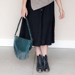 Woman holding a large teal leather fringe bag by its strap