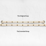 Two beige adjustable leather straps with brass grommets are displayed on a light textured background, labeled 'The Original Strap' and 'The Extended Strap'.