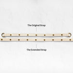 Two beige adjustable leather straps with brass grommets are displayed on a light textured background, labeled 'The Original Strap' and 'The Extended Strap'.