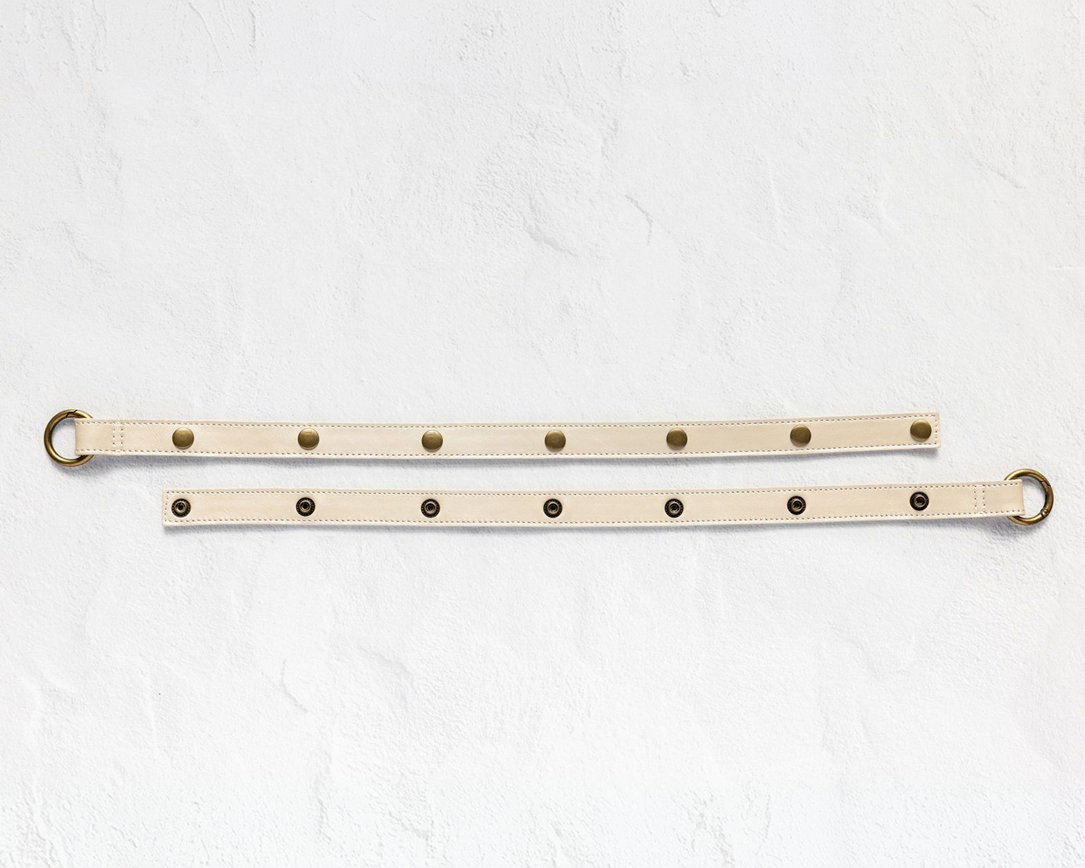 A beige leather belt with brass hardware, displayed in two parallel horizontal positions on a textured white background.