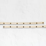 A beige leather belt with brass hardware, displayed in two parallel horizontal positions on a textured white background.