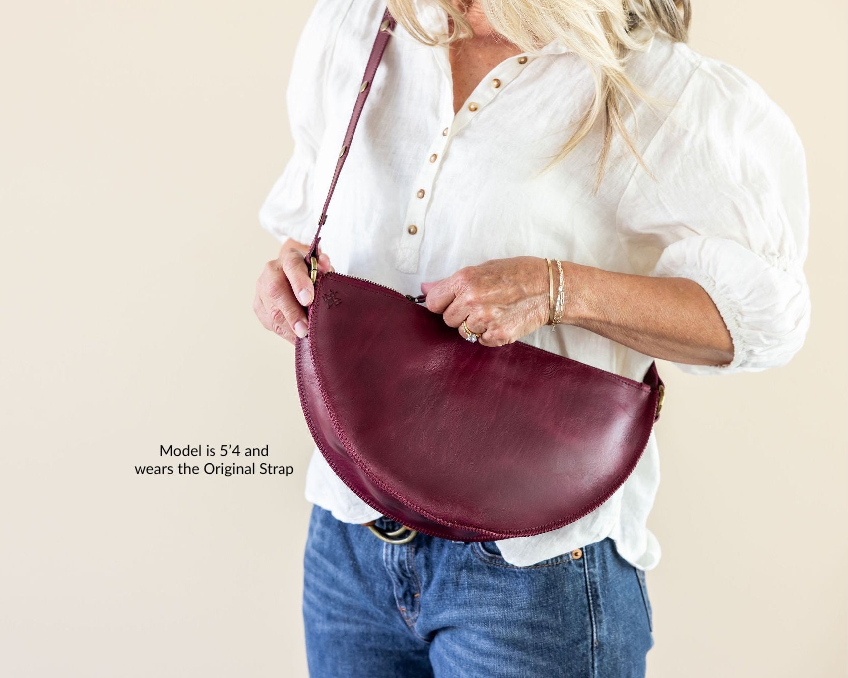 Person holding a burgundy handbag against a beige background