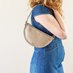 Person wearing a beige hat and blue jumpsuit with a beige handbag on a plain background