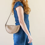 Woman wearing a blue dress and beige hat with a beige handbag against a plain background