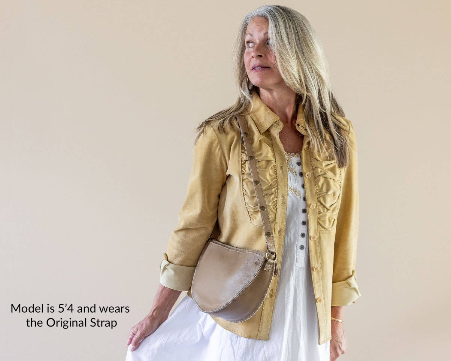 Woman wearing a yellow jacket and white dress with a beige bag against a plain background