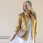 Woman wearing a yellow jacket and white dress with a beige bag against a plain background