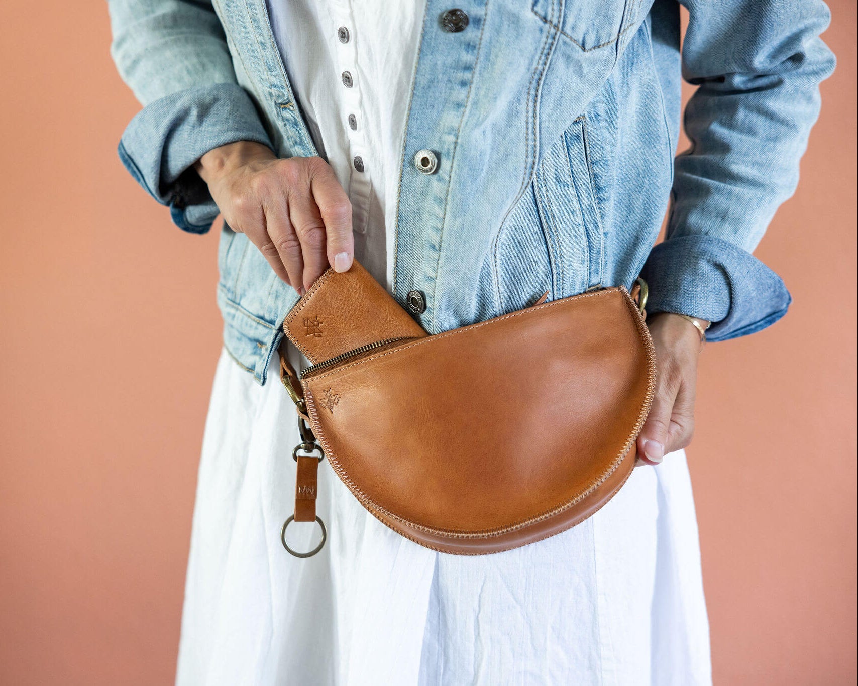 Person holding a brown leather saddle bag against a peach background