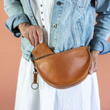 Person holding a brown leather saddle bag against a peach background