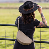 Person wearing a black hat and carrying a beige bag, standing in a field.