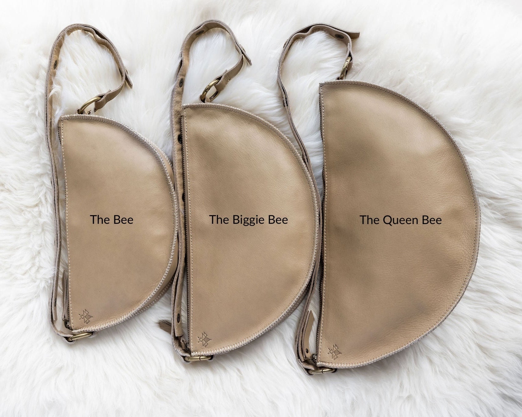 Three beige pouches labeled 'The Bee', 'The Biggie Bee', and 'The Queen Bee' on a white fur background.