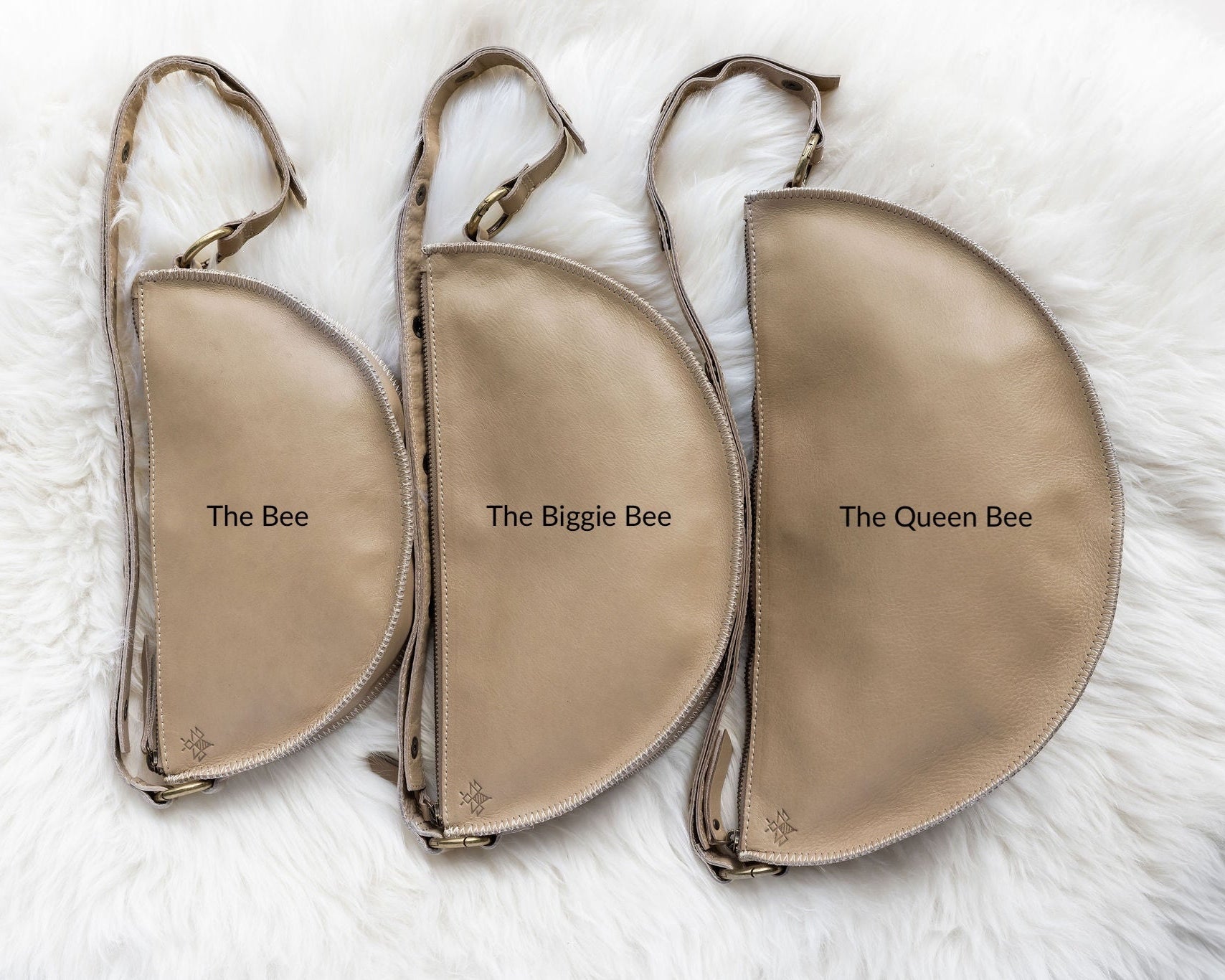 Three beige pouches labeled 'The Bee', 'The Biggie Bee', and 'The Queen Bee' on a white fur background.