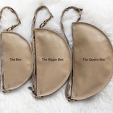 Three beige pouches labeled 'The Bee', 'The Biggie Bee', and 'The Queen Bee' on a white fur background.