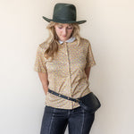 Woman wearing a patterned shirt, jeans, and a hat against a plain background
