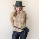 Woman wearing a patterned shirt, jeans, and a hat against a plain background