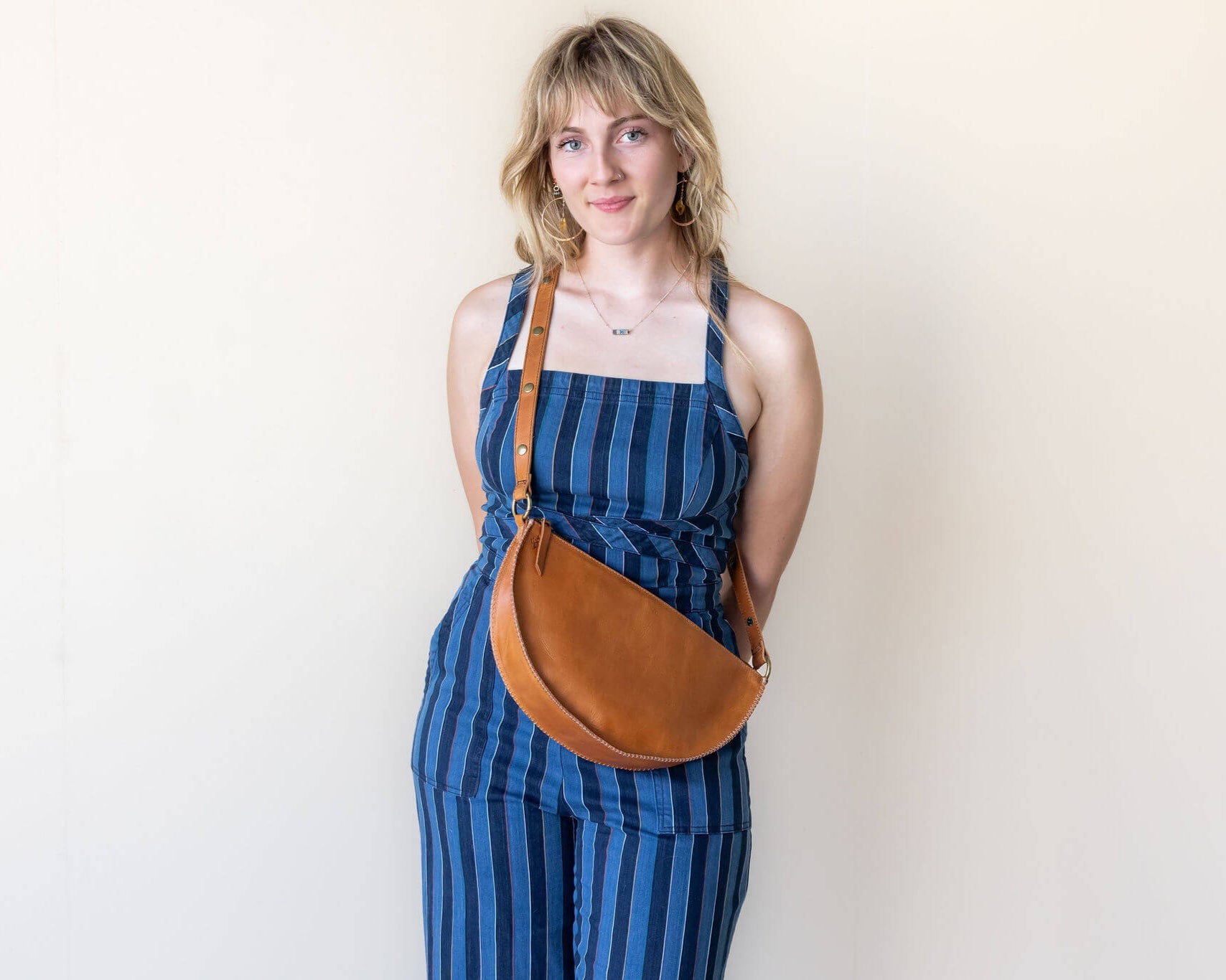 Woman wearing a blue striped dress with a brown leather bag against a plain background