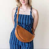 Woman wearing a blue striped dress with a brown leather bag against a plain background