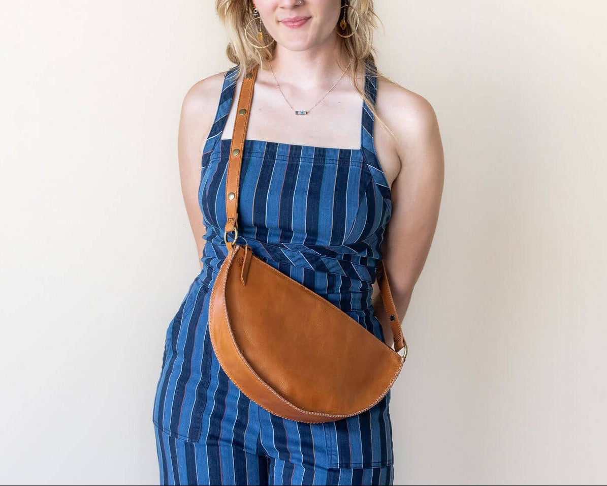 Woman wearing a blue striped dress with a brown leather bag against a plain background
