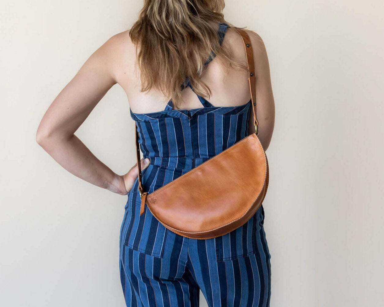 Woman wearing a blue striped dress with a brown leather bag on a plain background