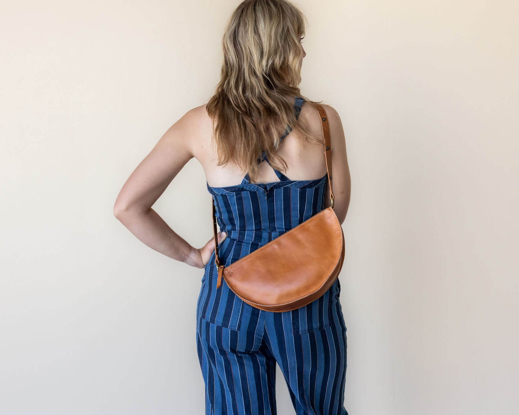 Woman wearing a blue striped dress with a brown leather bag on a plain background
