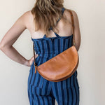 Woman wearing a blue striped dress with a brown leather bag on a plain background