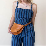 Woman wearing a blue striped jumpsuit with a brown leather belt bag against a plain background